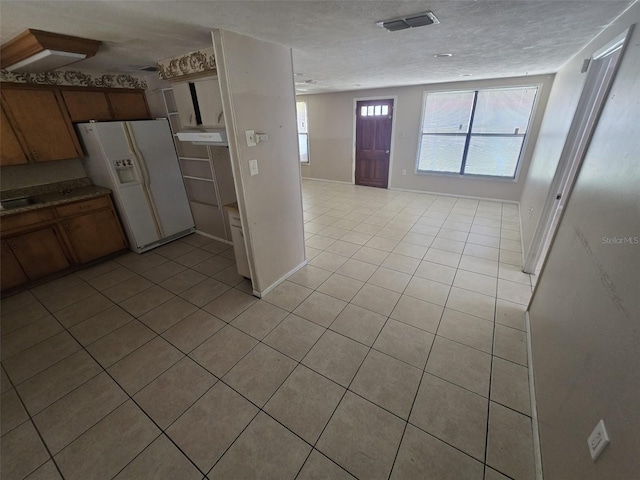 kitchen featuring white refrigerator with ice dispenser, light tile patterned floors, and plenty of natural light