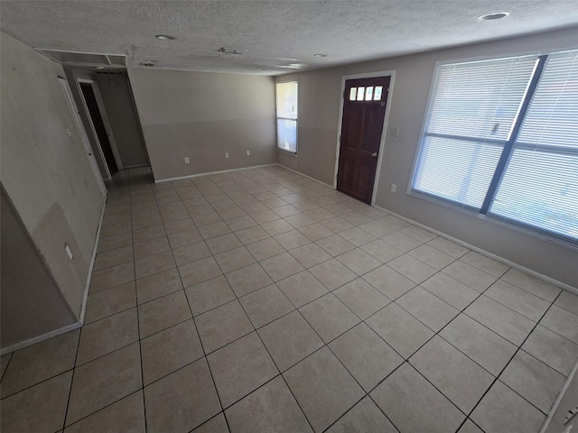 unfurnished living room featuring a textured ceiling, light tile patterned floors, and baseboards