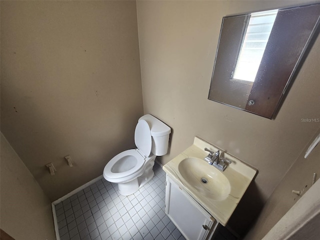 half bath with toilet, vanity, tile patterned floors, and baseboards