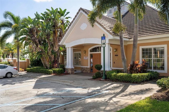 7628 Bay Port Rd Unit 43, Orlando, FL 32819 - property entrance featuring stucco siding, uncovered parking, a tiled roof, stone siding, and covered porch