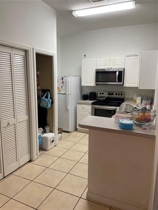 2882 Club Cortile Cir Unit B, Kissimmee, FL 34746 - kitchen with stainless steel appliances, white cabinetry, light tile patterned flooring, and lofted ceiling