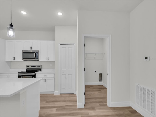 kitchen featuring appliances with stainless steel finishes, white cabinetry, light countertops, light wood-style flooring, and hanging light fixtures
