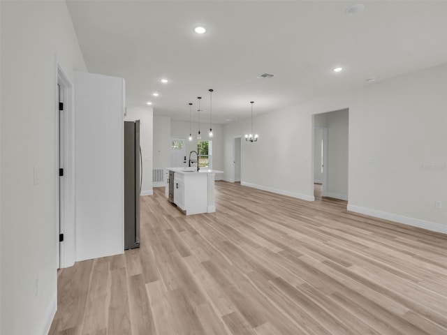 unfurnished living room featuring a sink, recessed lighting, light wood-style floors, baseboards, and a chandelier