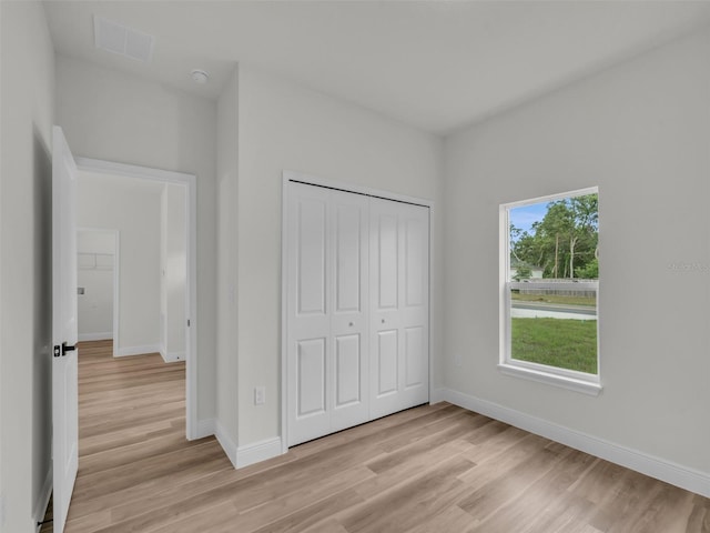 unfurnished bedroom featuring light wood-type flooring, baseboards, and a closet
