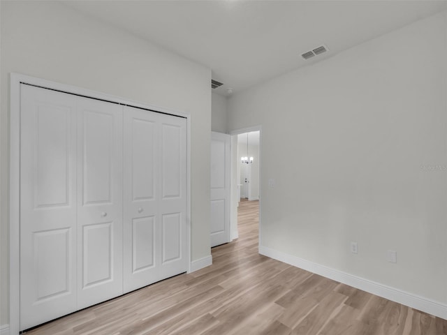unfurnished bedroom featuring light wood-style floors, baseboards, a closet, and a chandelier