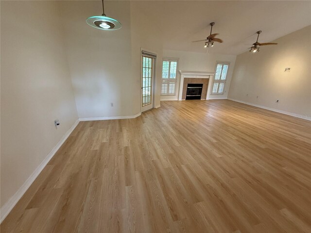 unfurnished living room with ceiling fan, baseboards, light wood finished floors, a tiled fireplace, and high vaulted ceiling