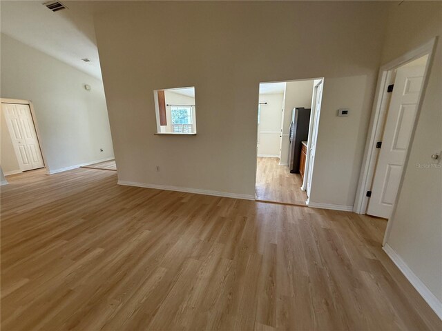 empty room featuring light wood finished floors, baseboards, and lofted ceiling
