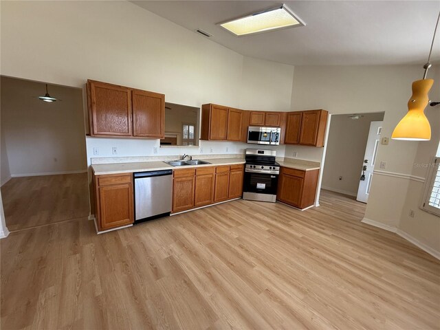 kitchen with stainless steel appliances, a sink, high vaulted ceiling, baseboards, and brown cabinetry