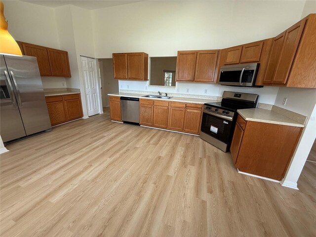 kitchen featuring stainless steel appliances, brown cabinets, light wood-type flooring, a towering ceiling, and light countertops