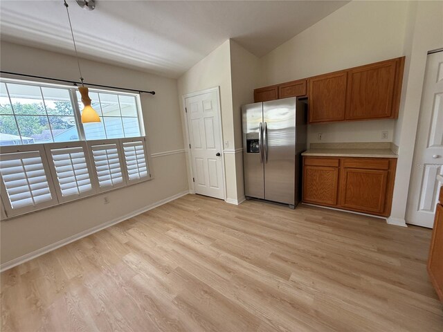 kitchen with stainless steel fridge with ice dispenser, lofted ceiling, brown cabinets, light wood finished floors, and light countertops
