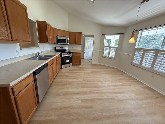 kitchen with appliances with stainless steel finishes, a sink, brown cabinetry, light wood-style flooring, and lofted ceiling