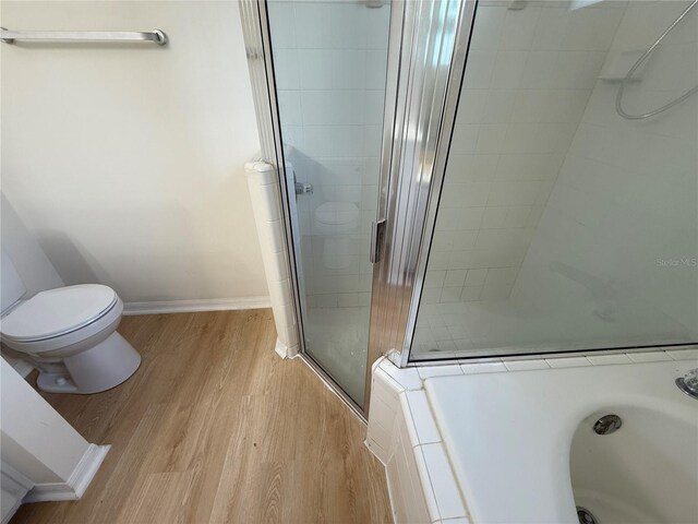 bathroom with wood finished floors, a stall shower, toilet, a bath, and baseboards