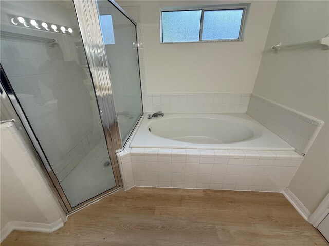 full bath featuring wood finished floors, a garden tub, a shower stall, and baseboards