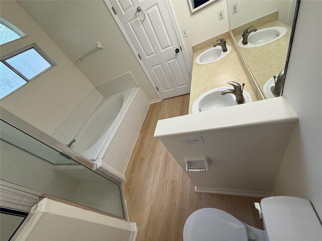 full bath featuring wood finished floors, toilet, a relaxing tiled tub, a shower, and double vanity