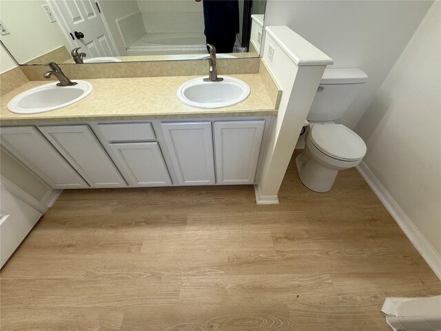 bathroom featuring wood finished floors, toilet, double vanity, and baseboards