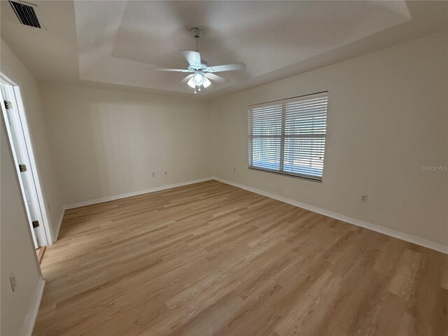 unfurnished room featuring ceiling fan, light wood finished floors, baseboards, and a tray ceiling