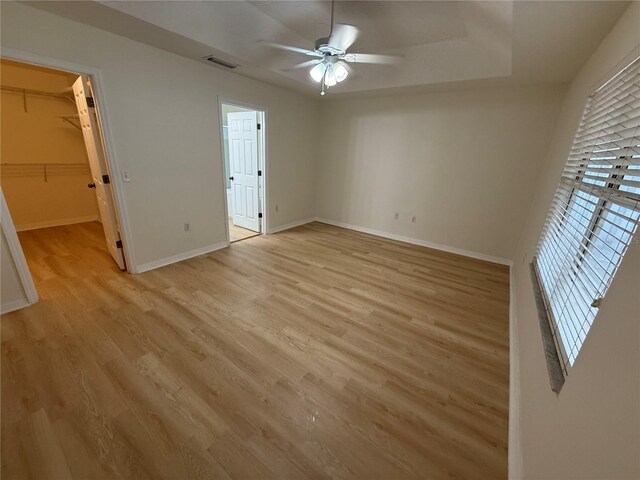 unfurnished bedroom with light wood-type flooring, baseboards, multiple windows, and a spacious closet