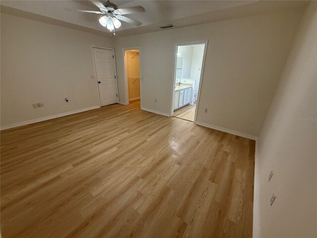 unfurnished bedroom featuring a spacious closet, baseboards, light wood-style flooring, ensuite bathroom, and a closet