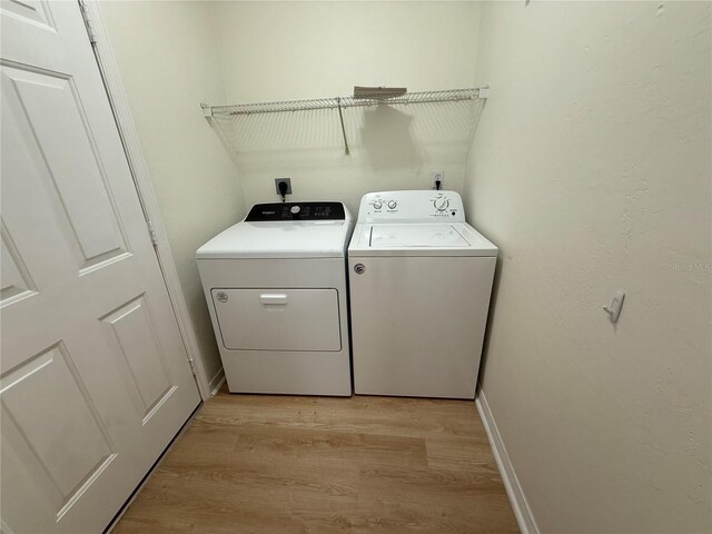 clothes washing area with separate washer and dryer, light wood finished floors, and baseboards