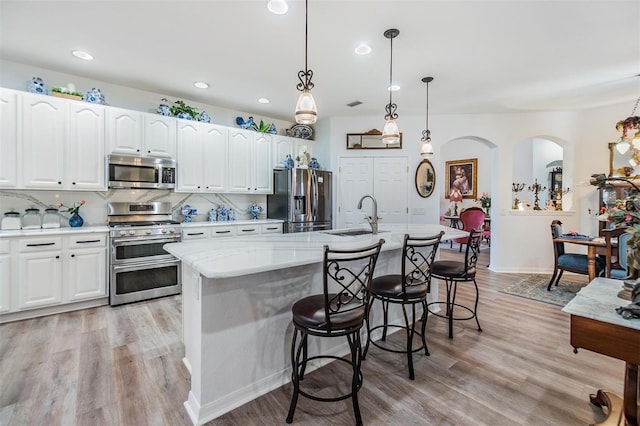 8721 Crystal Creek Ct, Land O Lakes, FL 34638 - kitchen featuring stainless steel appliances, a sink, a kitchen island with sink, white cabinets, and light wood-type flooring