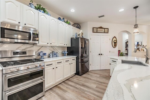 8721 Crystal Creek Ct, Land O Lakes, FL 34638 - kitchen featuring stainless steel appliances, a sink, arched walkways, light wood-style floors, and white cabinetry