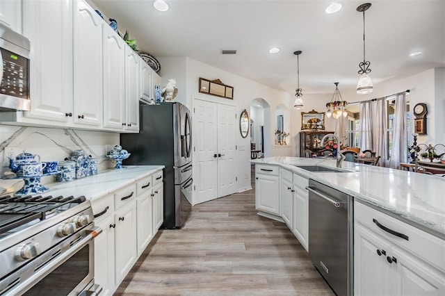 8721 Crystal Creek Ct, Land O Lakes, FL 34638 - kitchen with appliances with stainless steel finishes, a sink, arched walkways, white cabinetry, and light wood-style flooring