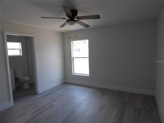unfurnished bedroom with wood finished floors, baseboards, connected bathroom, and ceiling fan