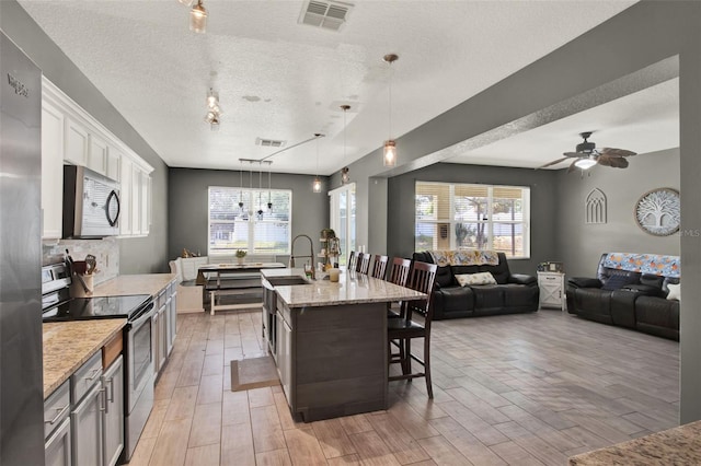 1744 Pine Ridge Dr, Davenport, FL 33896 - kitchen with stainless steel appliances, a textured ceiling, a sink, a breakfast bar, and light wood-style floors