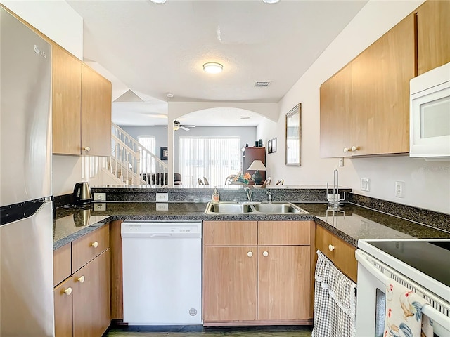 kitchen with white appliances, a sink, ceiling fan, a peninsula, and dark stone countertops