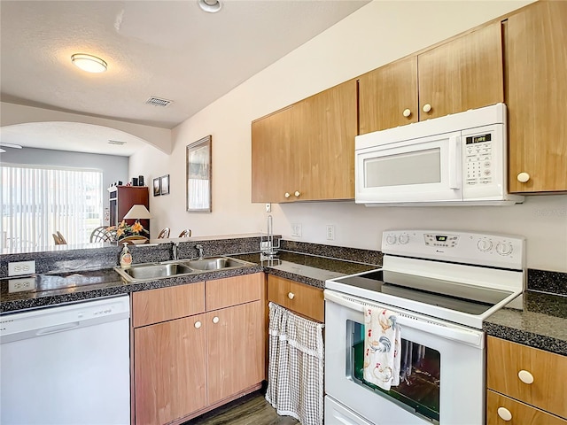 kitchen with white appliances, a sink, arched walkways, a peninsula, and wood finished floors
