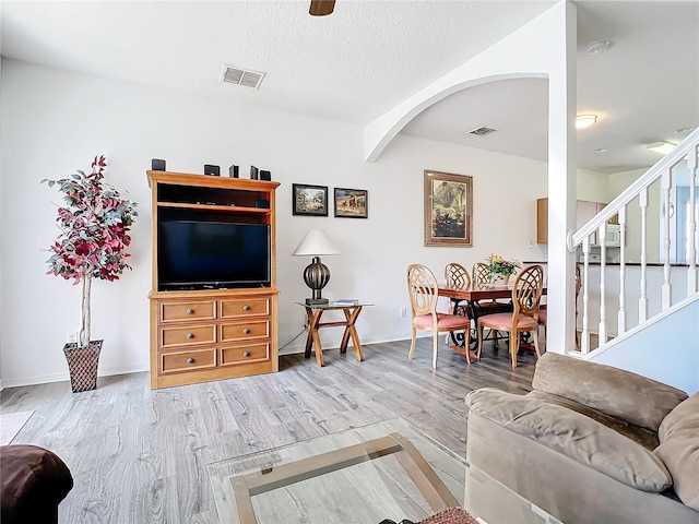 living area featuring wood finished floors, stairs, baseboards, and arched walkways