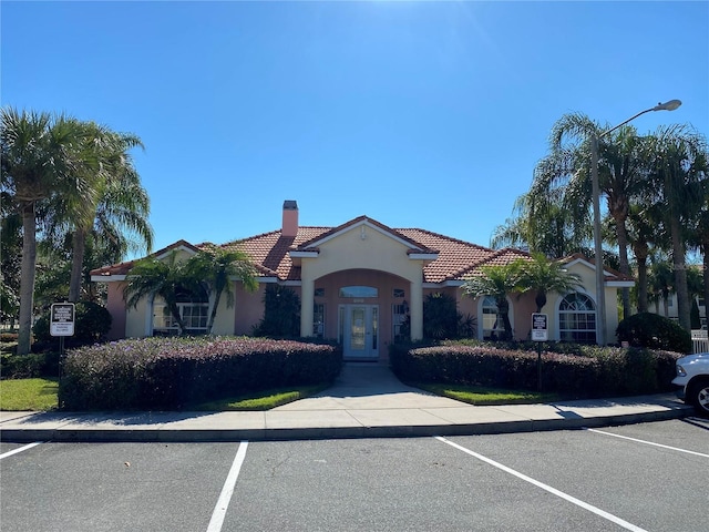 mediterranean / spanish home with stucco siding, uncovered parking, a chimney, and a tile roof