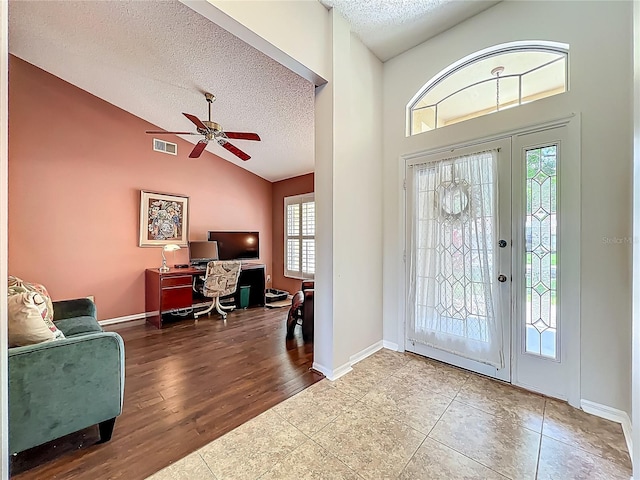 foyer entrance featuring a textured ceiling, a ceiling fan, tile patterned floors, baseboards, and high vaulted ceiling
