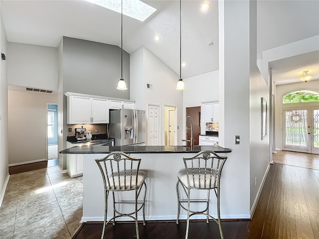 kitchen with stainless steel fridge, dark countertops, high vaulted ceiling, a skylight, and a breakfast bar area