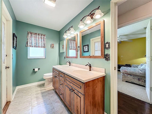 full bathroom featuring ensuite bathroom, a ceiling fan, double vanity, toilet, and baseboards