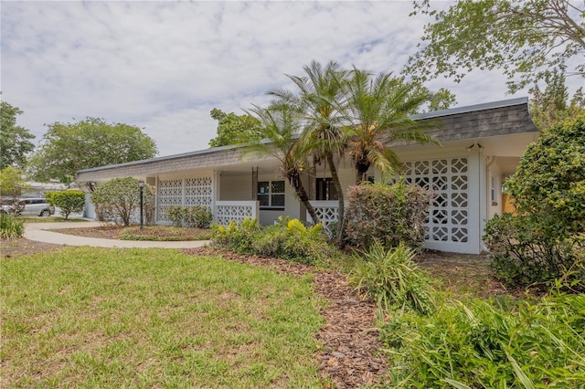 view of side of property featuring mansard roof, a lawn, a porch, and a shingled roof