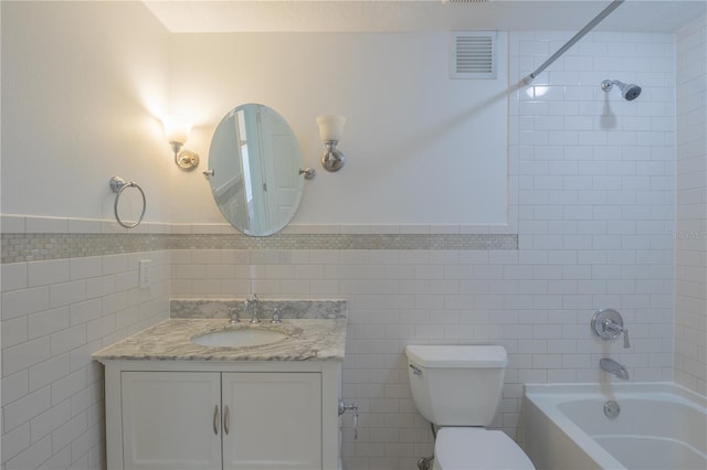 full bathroom with tile walls, bathtub / shower combination, vanity, toilet, and a wainscoted wall