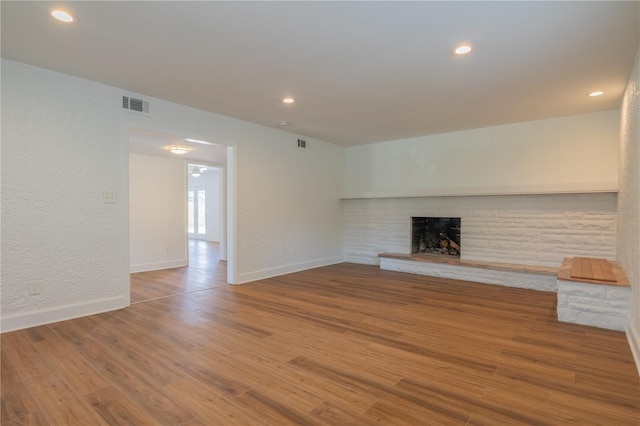 unfurnished living room with a fireplace, wood finished floors, baseboards, recessed lighting, and a textured wall