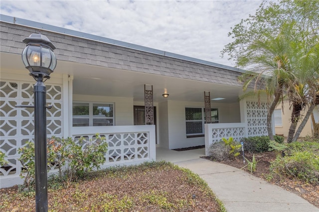 entrance to property featuring covered porch and roof with shingles