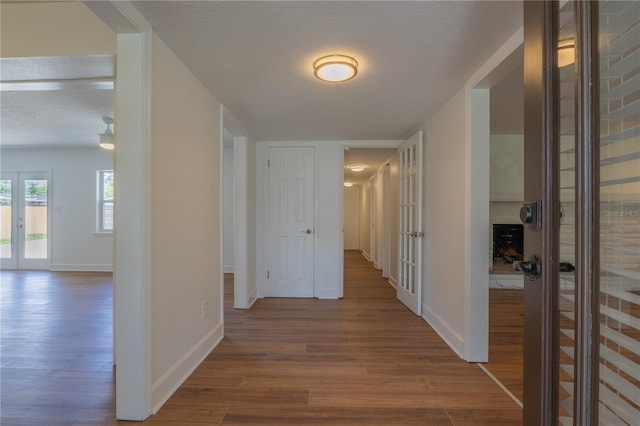 hall with french doors, wood finished floors, a textured ceiling, and baseboards
