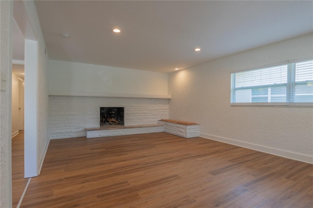 unfurnished living room featuring a brick fireplace, wood finished floors, baseboards, recessed lighting, and a textured wall