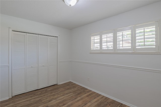 unfurnished bedroom featuring wood finished floors, baseboards, and a closet
