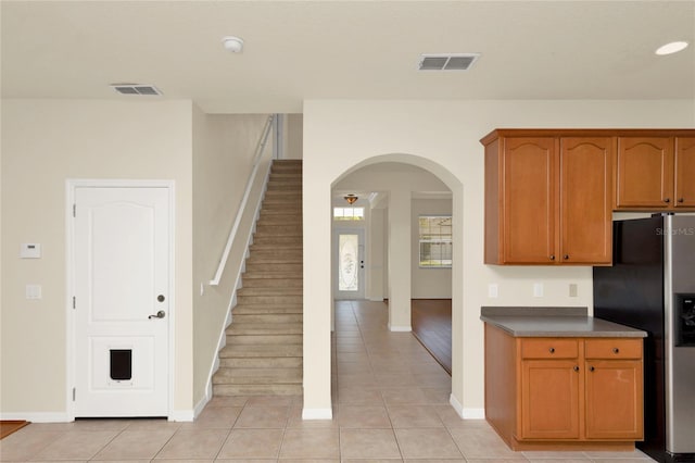 kitchen featuring stainless steel fridge with ice dispenser, light tile patterned floors, arched walkways, and baseboards