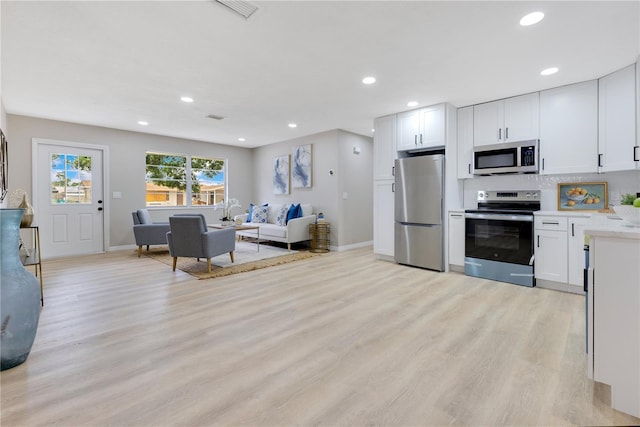 kitchen with appliances with stainless steel finishes, light wood-type flooring, open floor plan, white cabinets, and recessed lighting