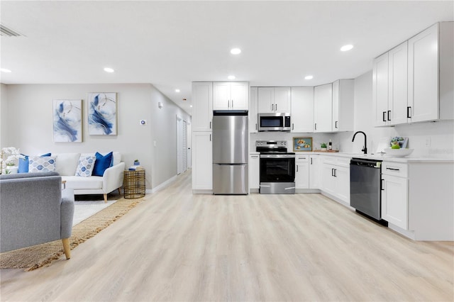 kitchen featuring appliances with stainless steel finishes, light wood-type flooring, open floor plan, recessed lighting, and white cabinets