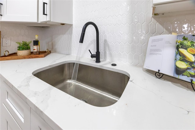 kitchen view of a sink, tasteful backsplash, white cabinetry, and light stone counters