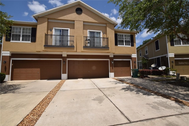 view of property featuring driveway, stucco siding, a garage, and a balcony