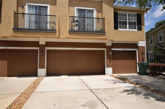 townhome / multi-family property with a balcony, stucco siding, an attached garage, and driveway