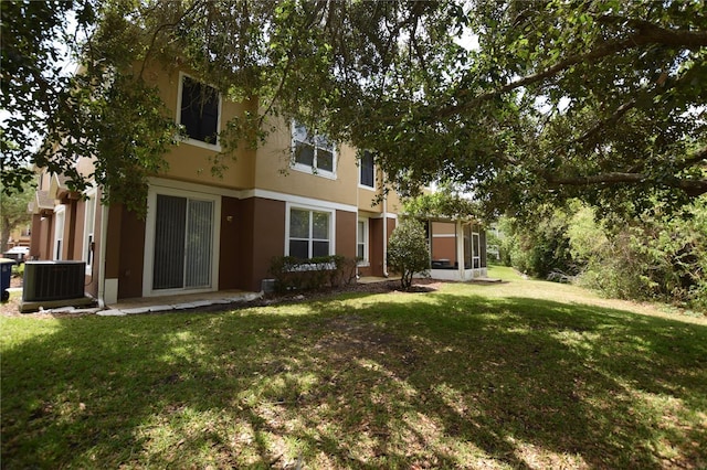 rear view of house featuring cooling unit, stucco siding, and a yard