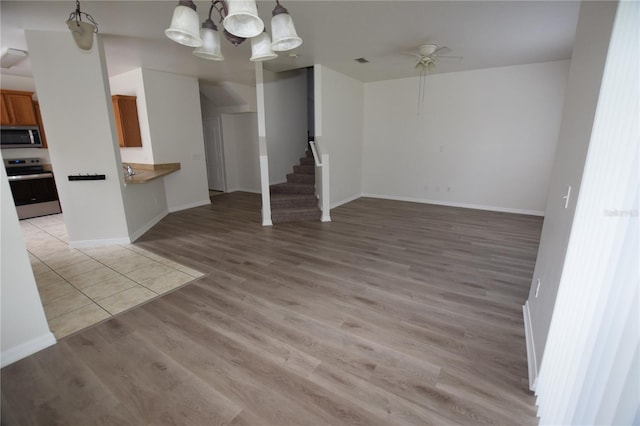 unfurnished living room featuring stairs, light wood-style flooring, a ceiling fan, and baseboards